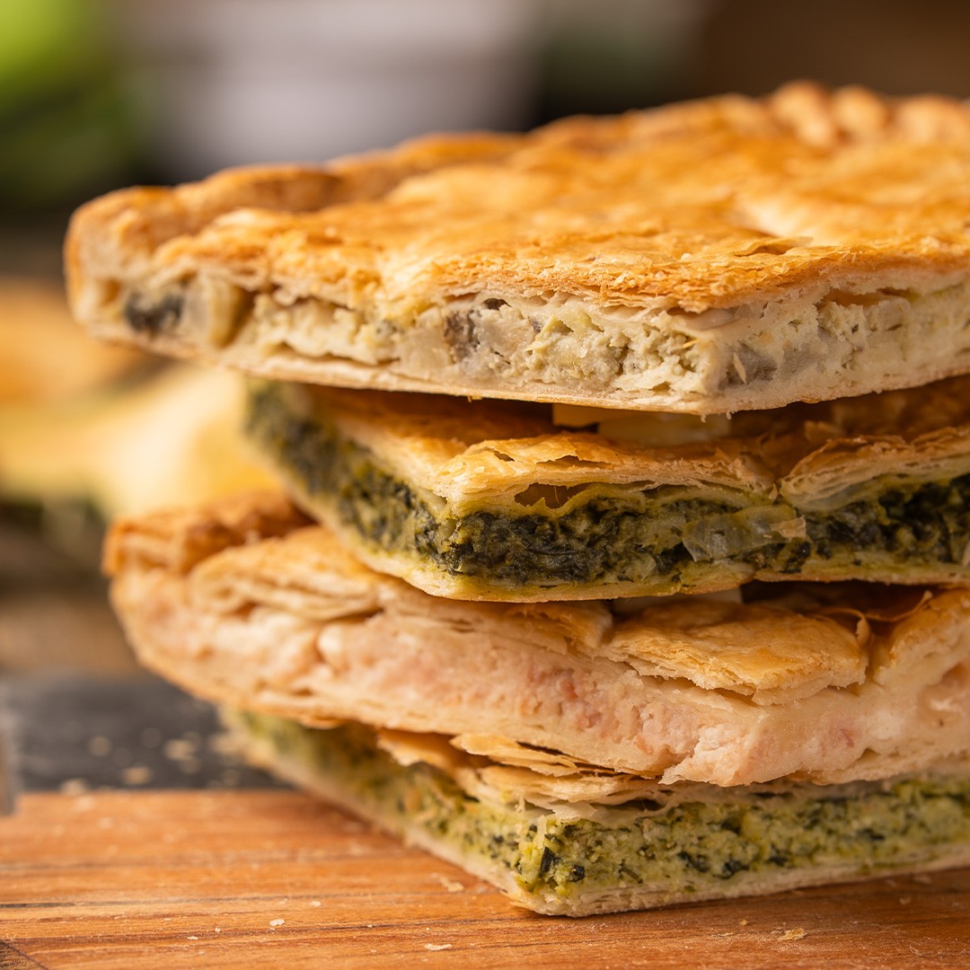 Cuadrados apilados de hojaldre dorado con relleno de espinaca y queso crema sobre tabla de madera