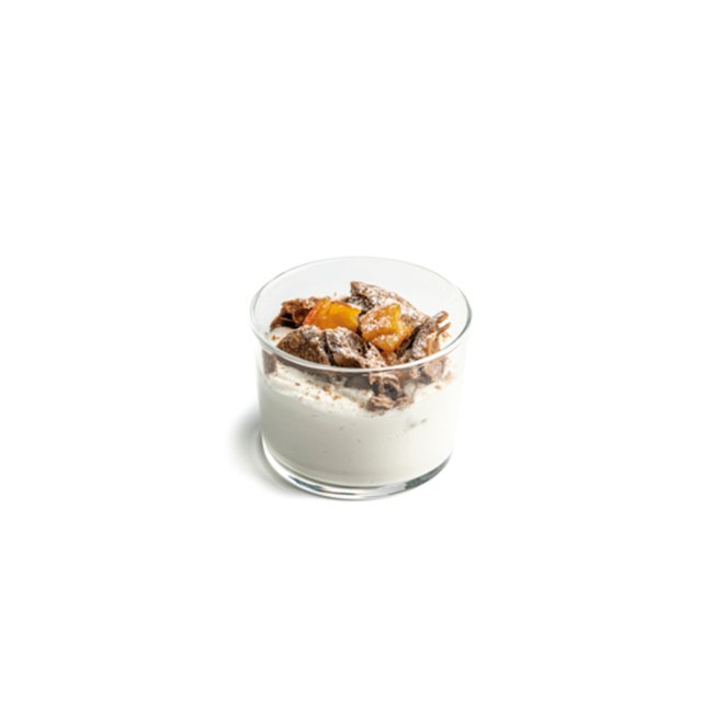 Copita de vidrio con yogur cubierto de granola y trocitos de melocotón, sobre fondo blanco
