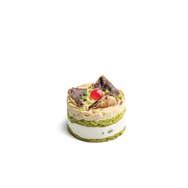 Pequeño pastel redondo con capas de pistacho verde y crema blanca, decorado con crema batida, cereza y chocolate